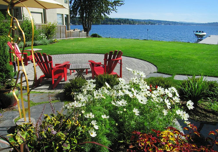 Landscaping and Consultations Bellevue Seattle - feature showing plantings, back patio with red chairs, lawn and water in back.